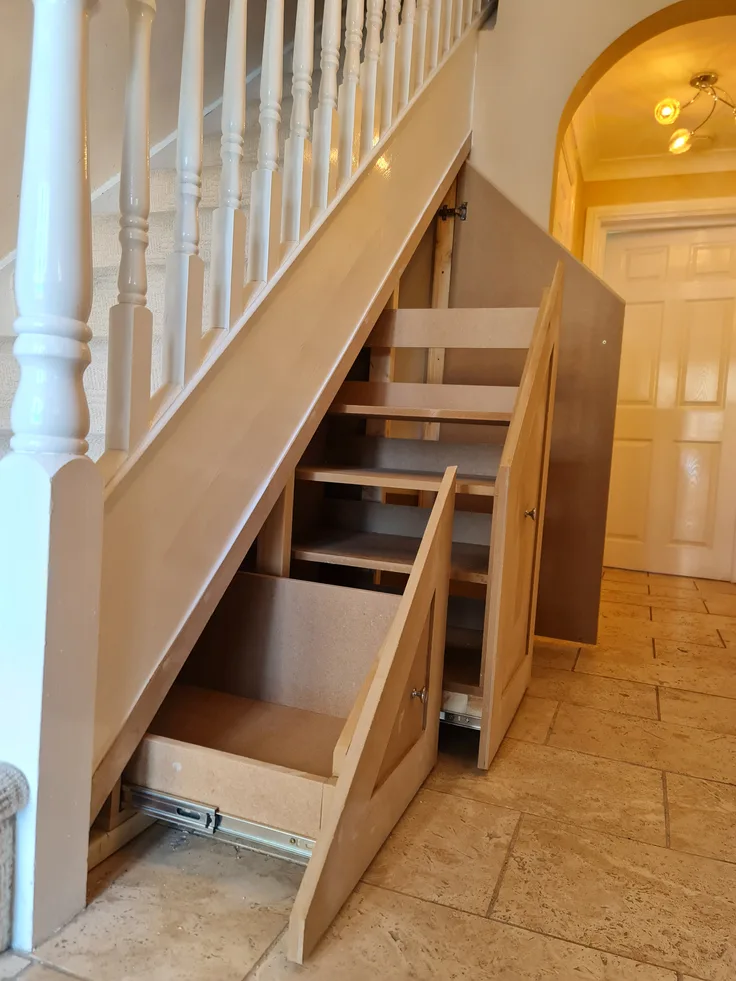 Crisp white bespoke under stairs pull-out shoe drawers and coat hooks