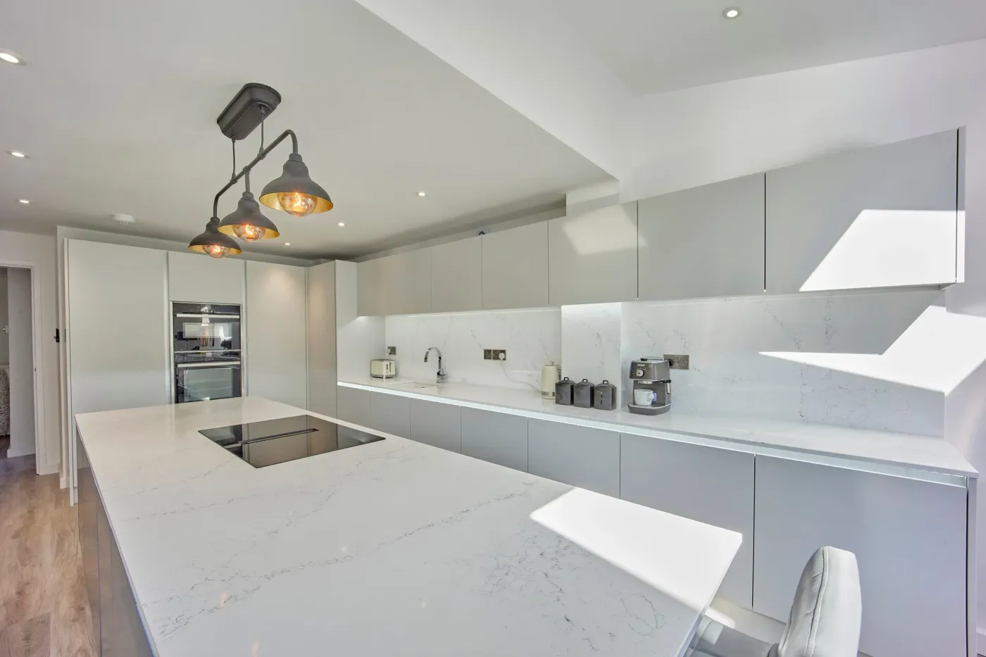 Handleless white kitchen installation with a marble-effect quartz island and breakfast bar