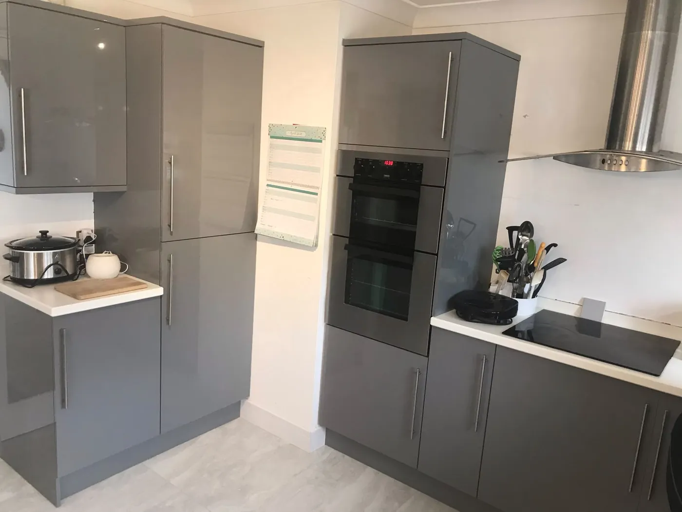 Grey gloss handleless kitchen with a built-in double oven, induction hob and chimney extractor