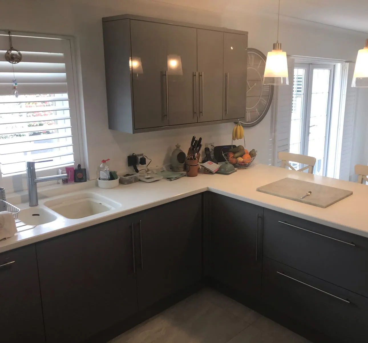 Grey L-shaped kitchen with a white solid-surface worktop, breakfast bar and pendant lights